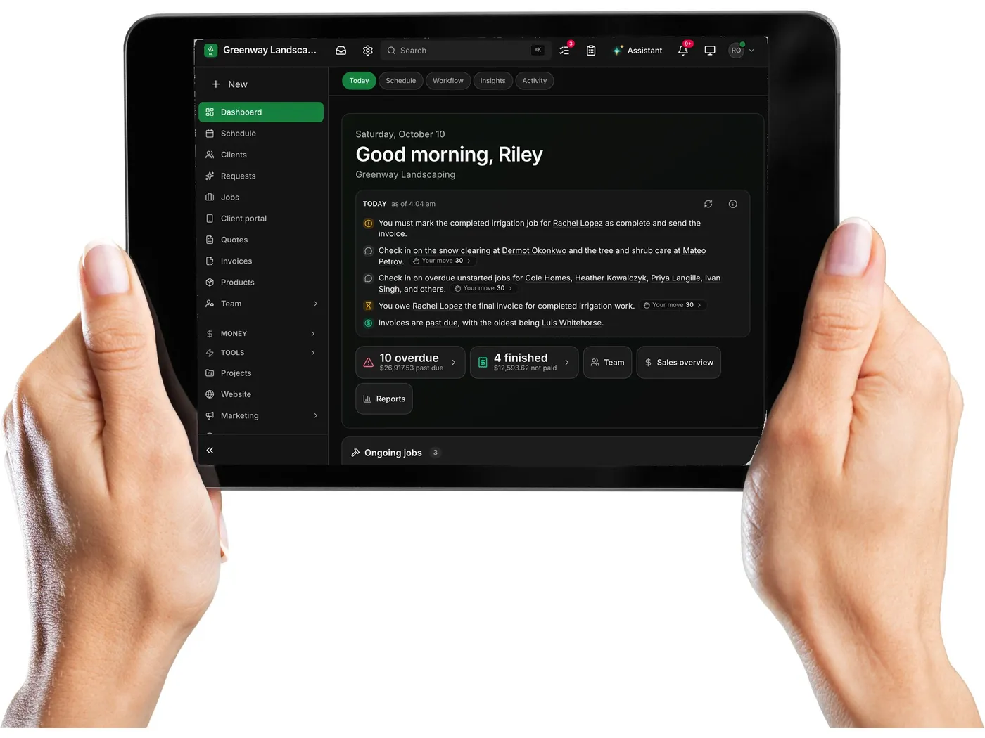 Two hands holding a tablet with a landscaping company’s Daybook dashboard on it: good morning, today’s list, ten invoices overdue and four jobs finished but not paid.