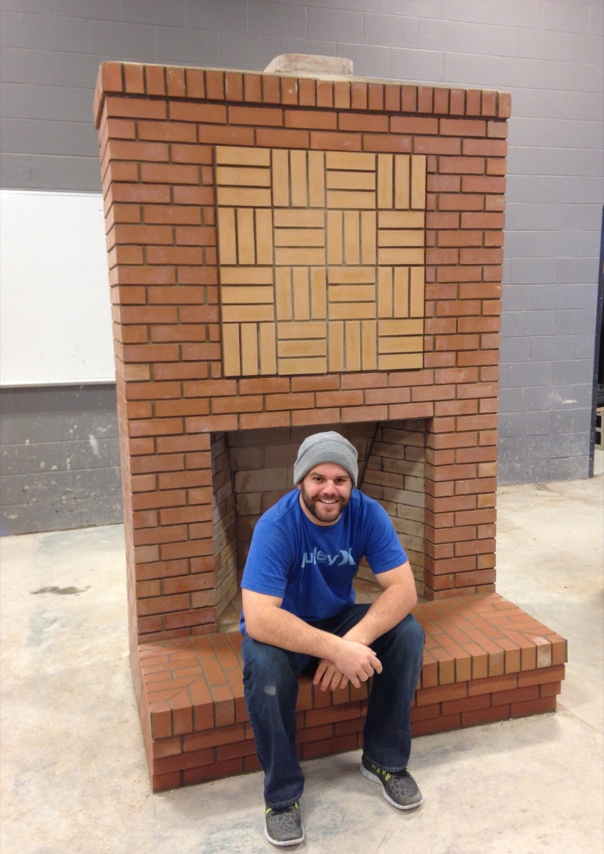 Ryan seated in the hearth of a brick fireplace he built — his Red Seal final exam.
